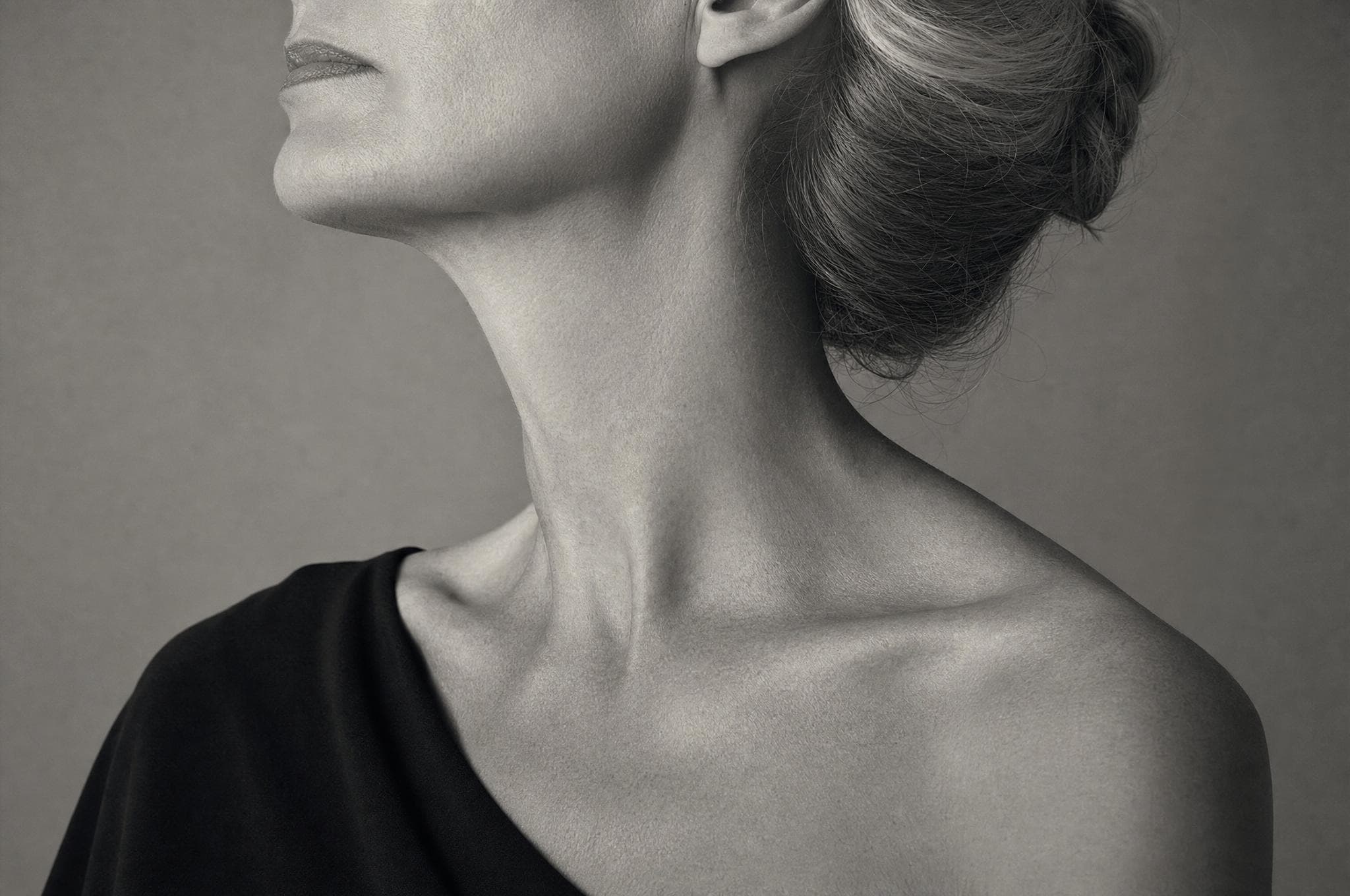 The curve of a woman's neck and jaw, hair in a low chignon, seen from behind