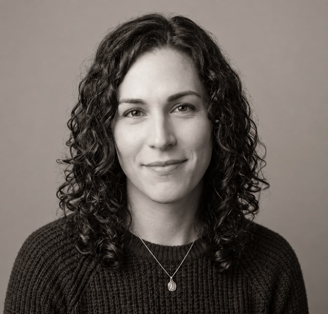 Black-and-white portrait of a woman with dark curly hair in a dark knit sweater, looking at the camera with a slight smile
