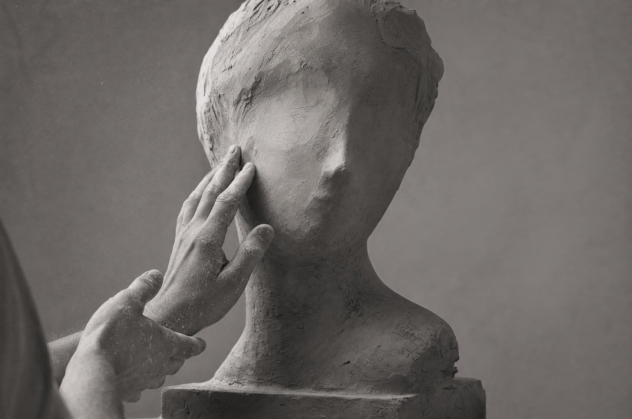 A sculptor's hands refining an unfinished clay bust